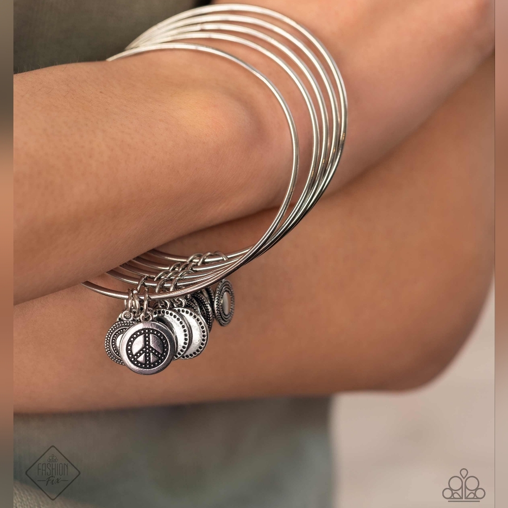 Silver discs, adorned in radiating textures, slide along a stack of silver bangl